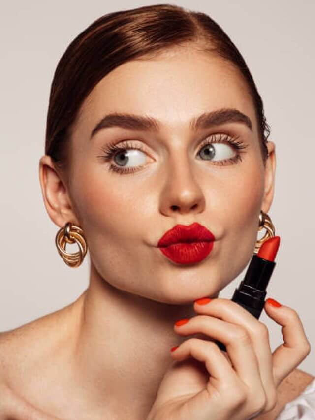 Beautiful emotional woman with bright make-up applying red lipstick