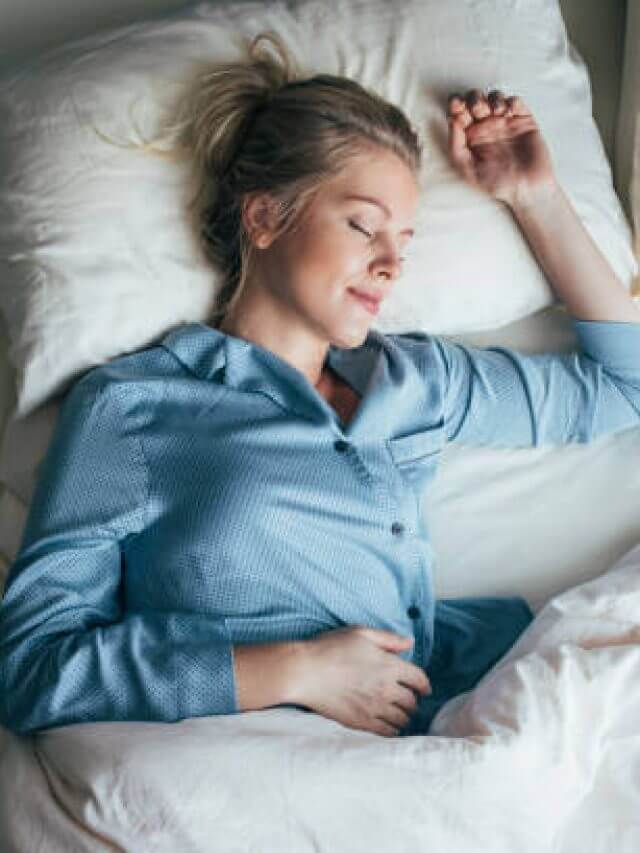 Beautiful happy Caucasian woman in blue pyjamas sleeping on a king-size bed.