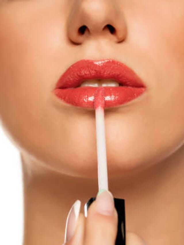 Closeup of woman applying a lip gloss on her lips on a white background