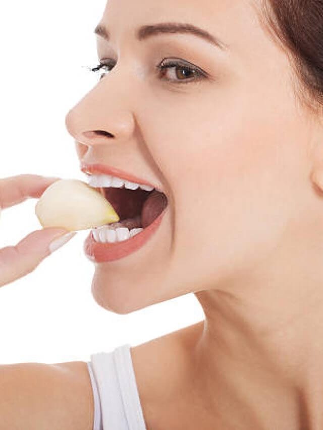 Beautiful woman eating garlic. Isolated on white.