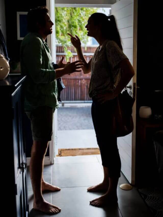 Silhouette of unhappy couple arguing standing at house door.