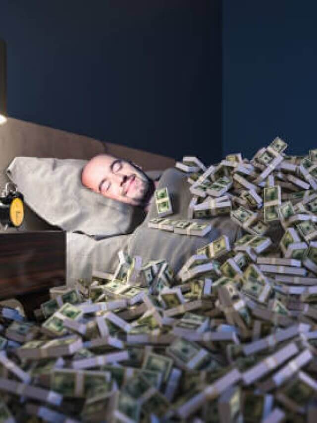 Smiling man sleeping in a bed covered with dollars money. wealth concept.