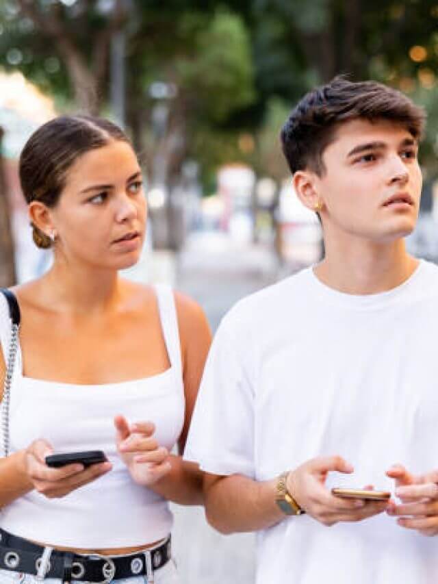 Modern young man and woman strolling together and phubbing