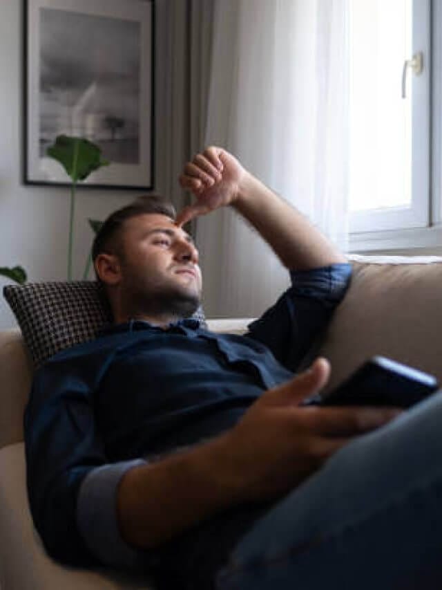 Thoughtful serious man sitting on sofa at home, lost in thoughts
